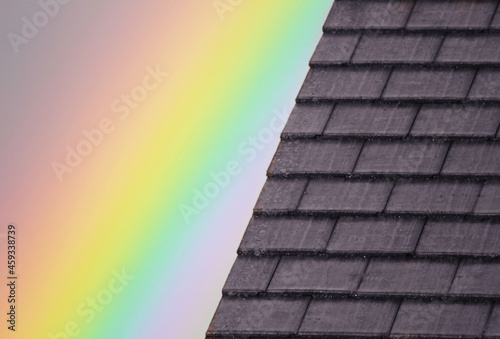 Bright rainbow over the dark roof of a house building. Nature contrast