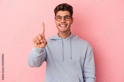 Young caucasian man isolated on pink background showing number one with finger.