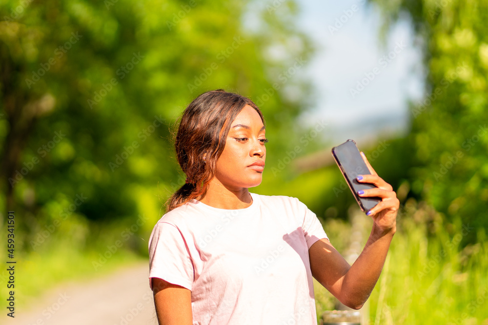 Young black woman with her phone taking selfie in a park on an October afternoon. Young black woman with her phone taking selfie in a park on an October afternoon.
