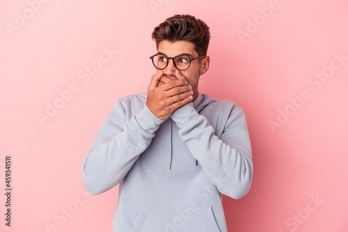 Young caucasian man isolated on pink background thoughtful looking to a copy space covering mouth with hand.