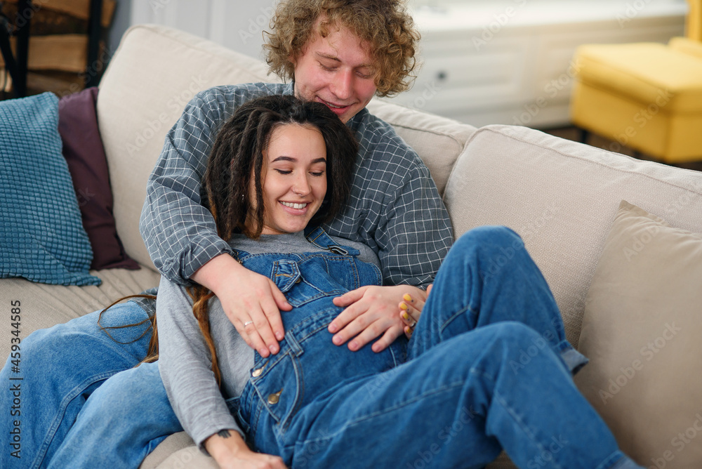 © gorynvd - Husband touching pregnant tummy of his charming joyful wife which lying on the couch in cozy living room © gorynvd - Husband touching pregnant tummy of his charming joyful wife which lying on the couch in cozy living room