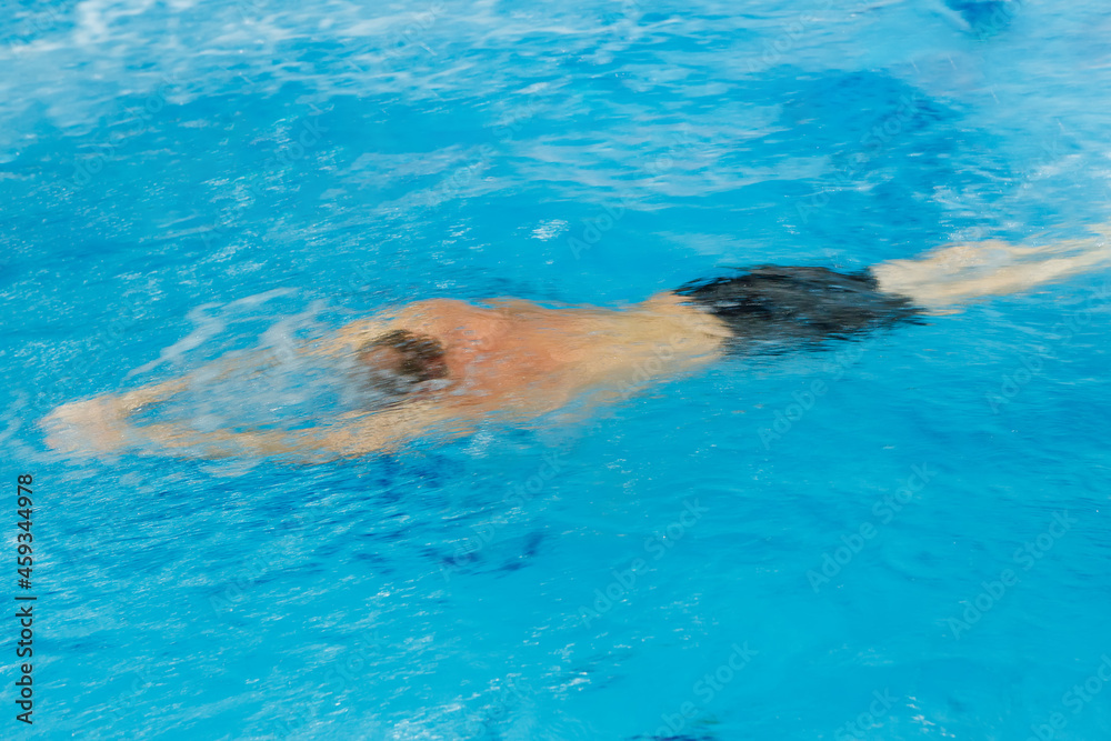 A swimmer swims quickly under the water in the pool. Blurry movement.