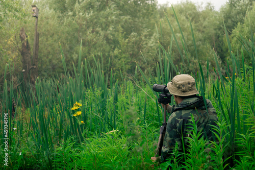 male explorer makes observations in the wild with a spotting scope standing among the tall grass