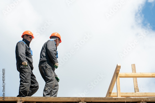 Repair of a wooden roof outdoors against a blue sky background. Two carpenters in special clothes work at a height. Roofing contractors are preparing the roof for the installation of insulation