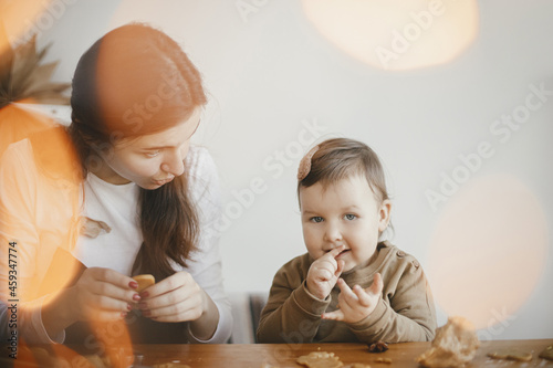 Family holiday preparations. Cute daughter and mother making christmas cookies on messy table, close up. Adorable toddler girl with mom cutting dough for gingerbread cookies. Moments together
