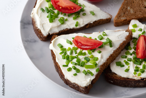 Slices of bread with cottage cheese, onion and tomatoes on wooden plate on white background