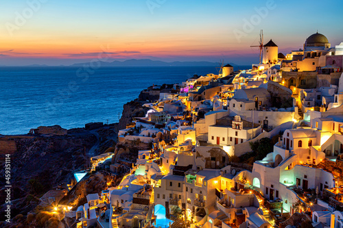 Greece vacation background. Famous iconic Oia village with traditional white houses and windmills during colorful sunset. Santorini island, Greece.
