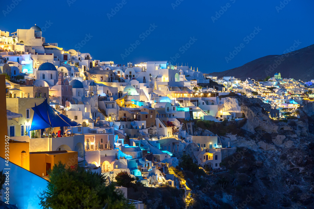 Famous Oia village with white houses and blue dome churches during sunset on Santorini island, Aegean sea, Greece.