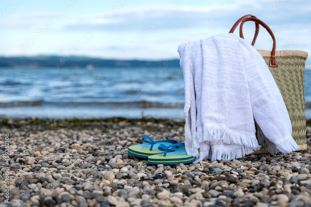 wicker basket, towel and slippers on a rocky beach against a beautiful sky wicker basket, towel and slippers on a rocky beach against a beautiful sky