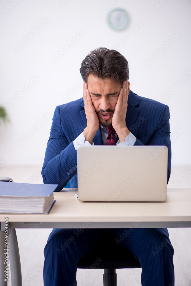 Young male employee unhappy with excessive work in the office Young male employee unhappy with excessive work in the office