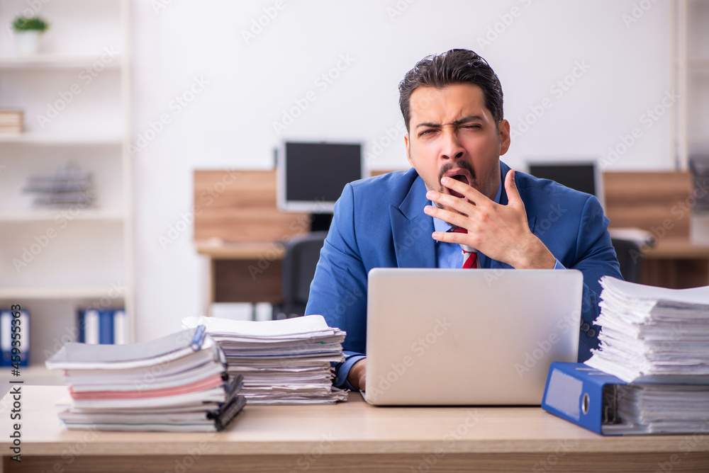 Young male employee unhappy with excessive work at workplace Young male employee unhappy with excessive work at workplace