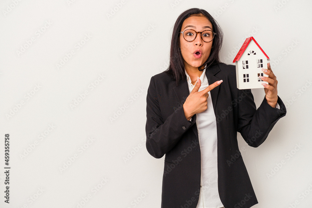 Young business latin woman holding a toy house isolated on white background pointing to the side Young business latin woman holding a toy house isolated on white background pointing to the side