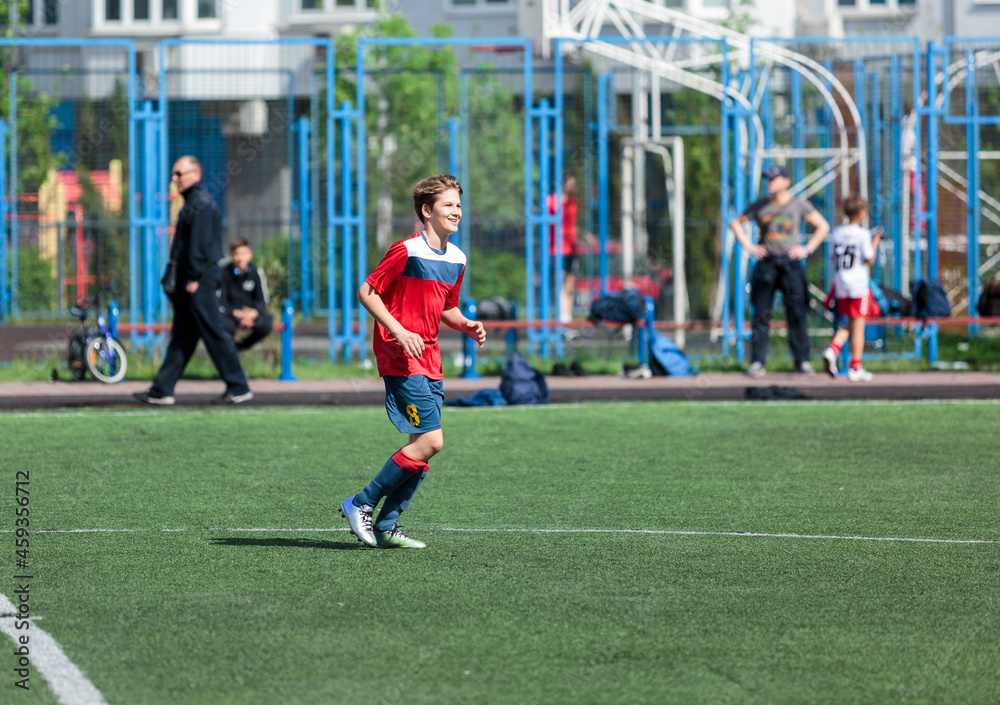 Obraz premium Young sport boys in red sportswear running and kicking a ball on pitch. Soccer youth team plays football in summer. Activities for kids, training