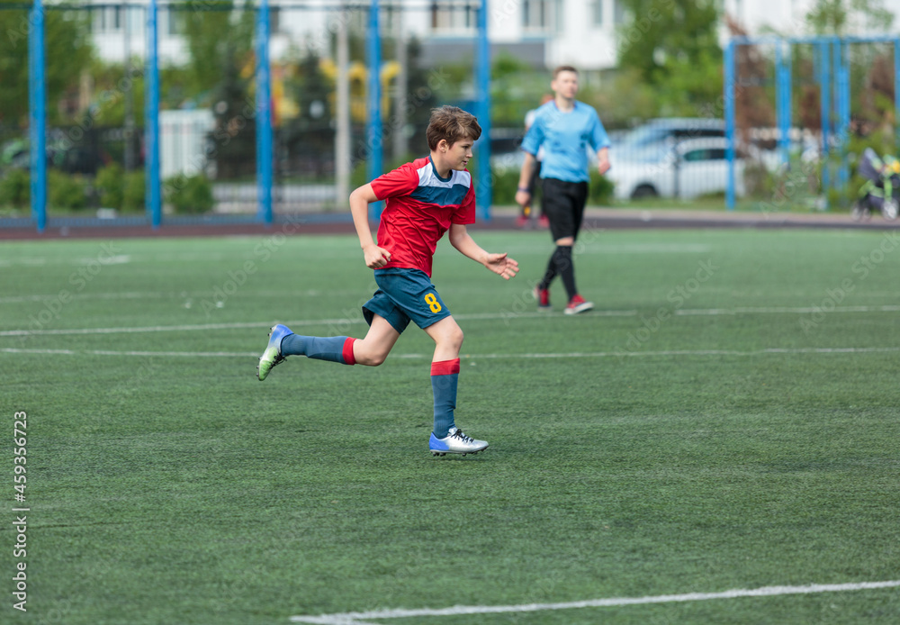 Young sport boys in red sportswear running and kicking a  ball on pitch. Soccer youth team plays football in summer. Activities for kids, training	