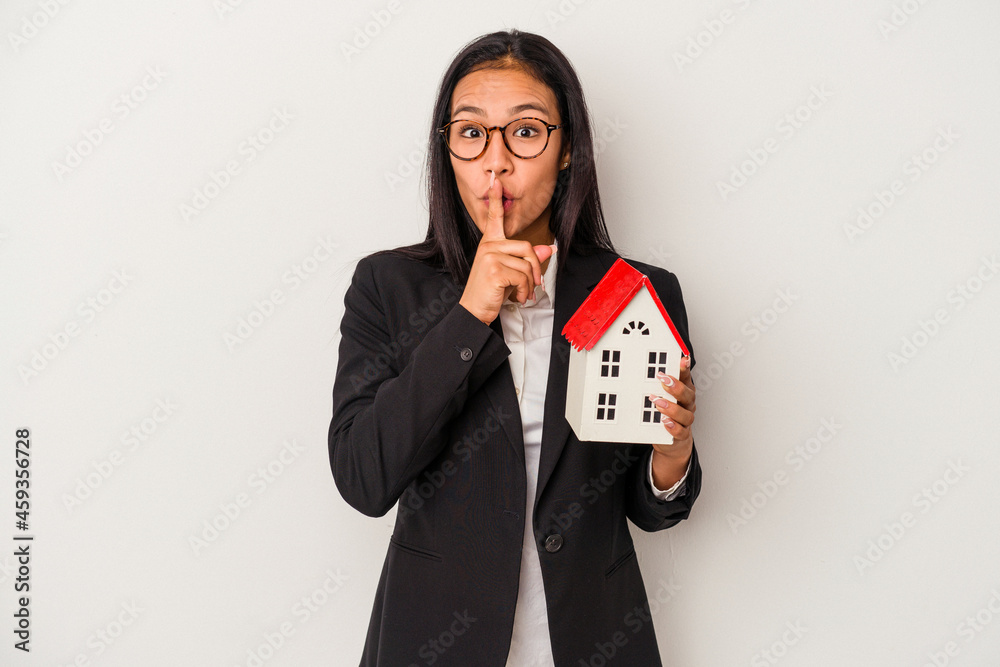 Young business latin woman holding a toy house isolated on white background keeping a secret or asking for silence. Young business latin woman holding a toy house isolated on white background keeping a secret or asking for silence.