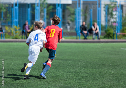 Young sport boys in red sportswear running and kicking a ball on pitch. Soccer youth team plays football in summer. Activities for kids, training © Natali