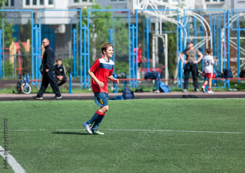 Young sport boys in red sportswear running and kicking a  ball on pitch. Soccer youth team plays football in summer. Activities for kids, training  © Natali