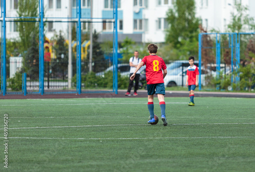 Young sport boys in red sportswear running and kicking a  ball on pitch. Soccer youth team plays football in summer. Activities for kids, training  © Natali