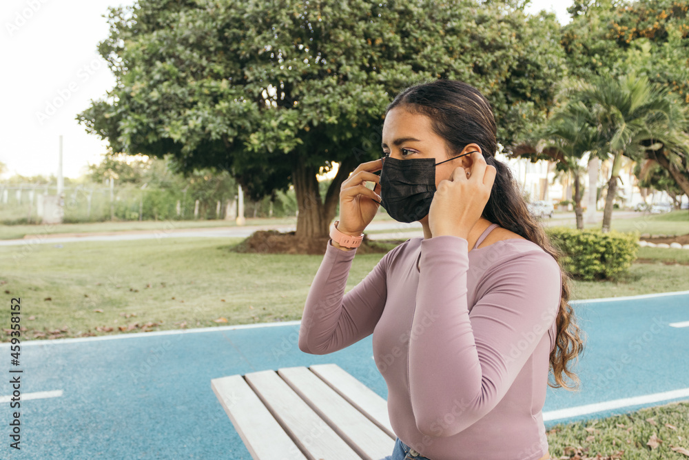 Hispanic young woman wearing face mask while getting ready to do exercise at a park