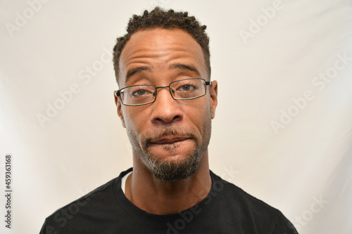African American male wearing glasses looks into the camera while biting his lip. 