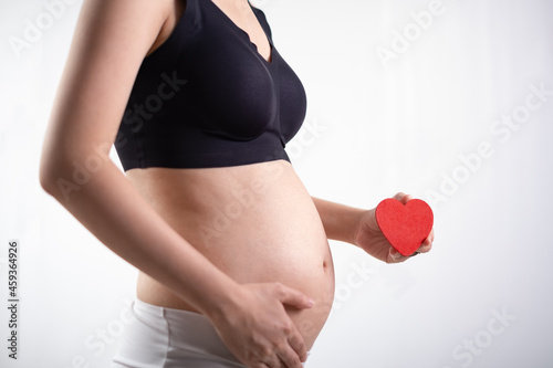 Pregnant woman in white and black underwear. Young woman expecting a baby. Side view hand holding red heart.