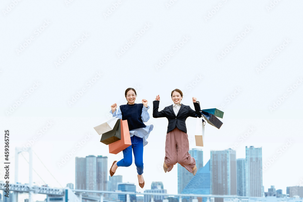 買い物袋を沢山持ってジャンプする女性2人（セール・爆買い）