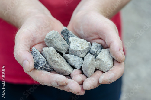 The man holds the rubble in his palms. Pieces of random granite stones. Close-up. Selective focus. Outside the room.