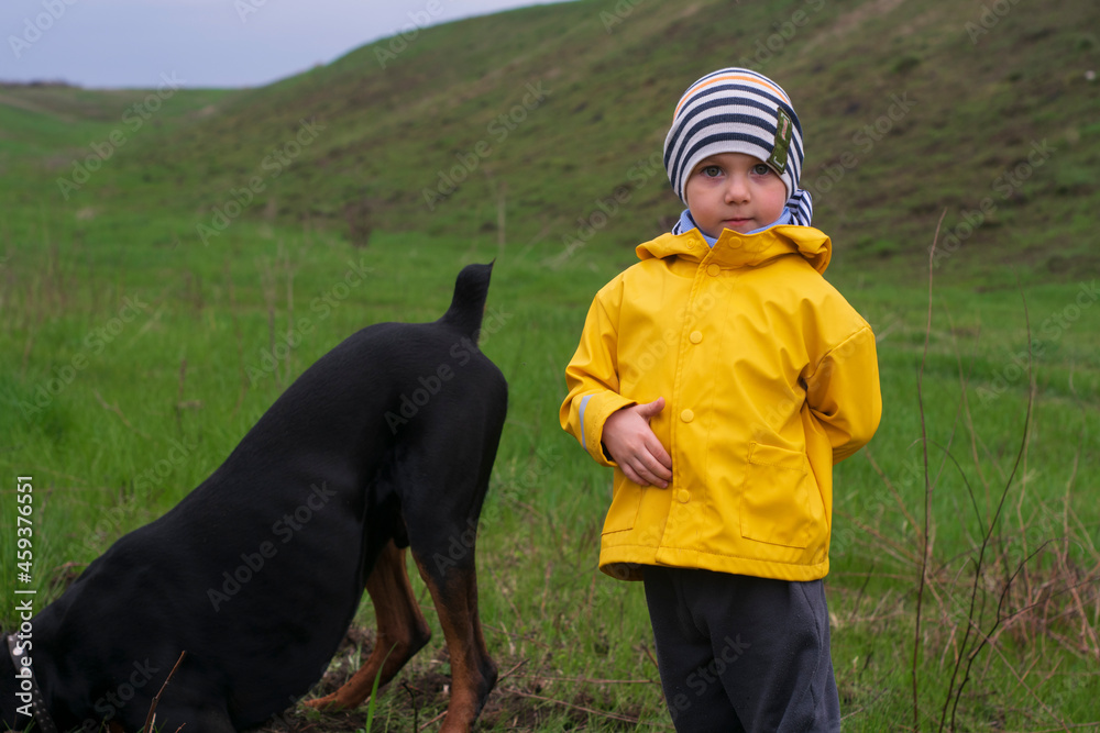 Blond boy in a yellow jacket stands on a green meadow Blond boy in a yellow jacket stands on a green meadow