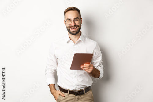 Confident business man holding digital tablet and smiling, standing against white background photo