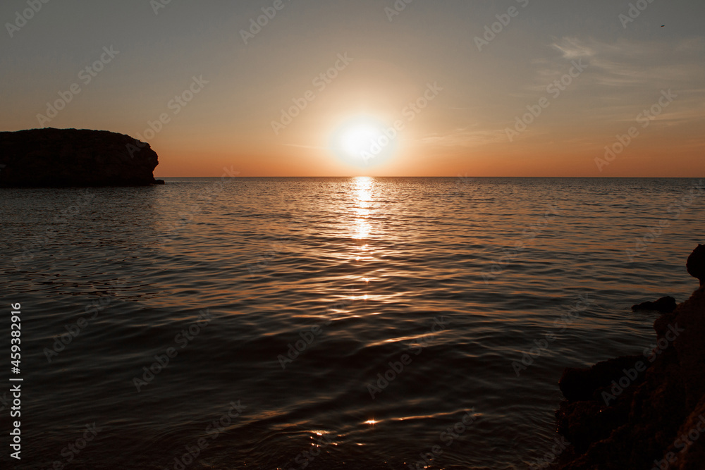 waves wash the rocky shore of the sea. Sunset. Reflection in the water of the bridge and rays