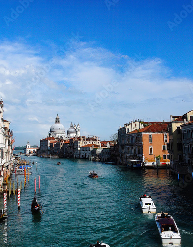 The Grand Canal in Venice, Italy.  There are palaces, speedboats and a gondola in the foreground and the Basilica di Santa Maria della Salute is seen in the distance.  Modern colors. © Andrea DiSavino