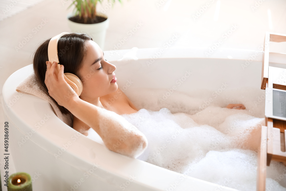 Naklejka premium Young woman listening to music while taking bath at home