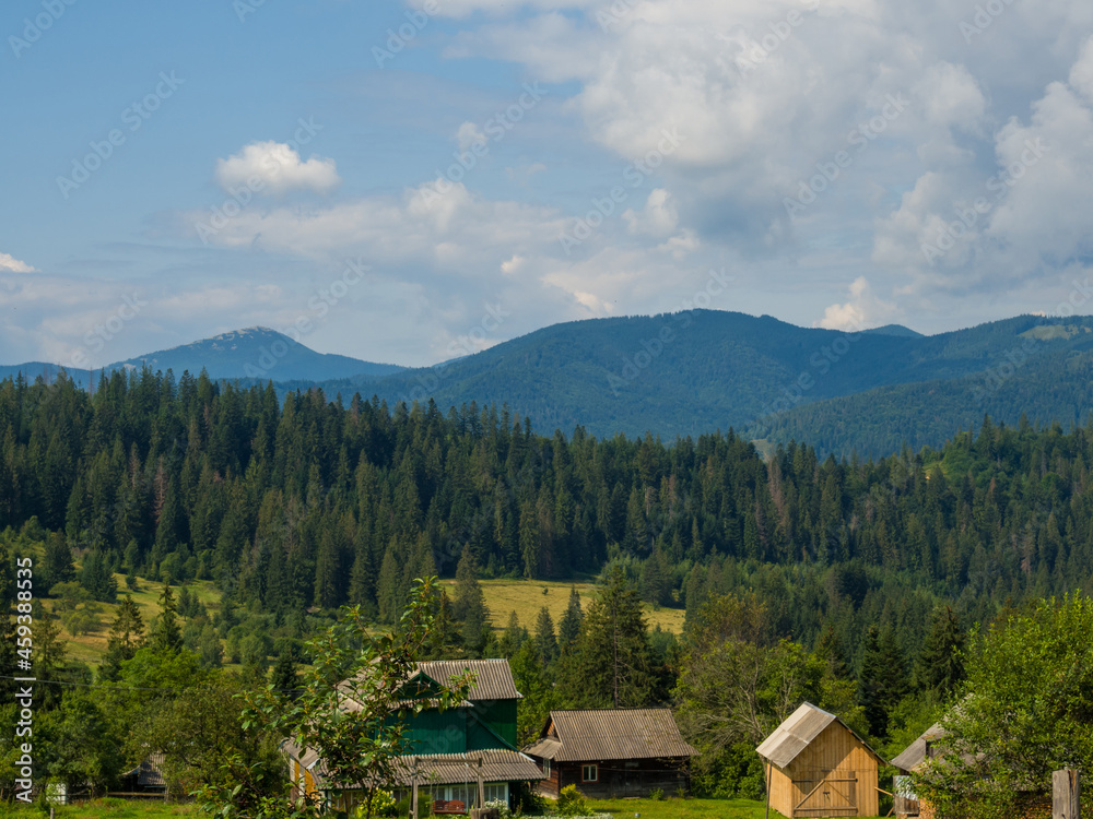 Carpathian landscape with cloudy sky. A wooden house on a green meadow in mountains near old forest. Lifestyle in the Carpathian village. Ecology protection concept. Explore the beauty of the world.