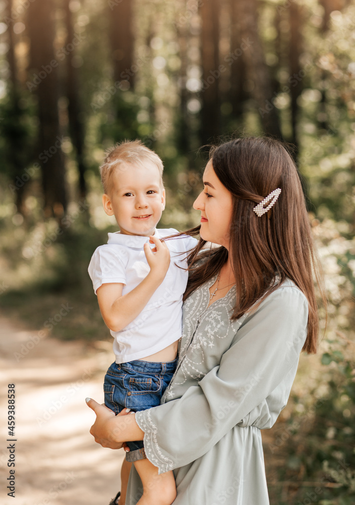 A young beautiful mother holds her young son in her arms and plays with him in the summer in nature. A young beautiful mother holds her young son in her arms and plays with him in the summer in nature.