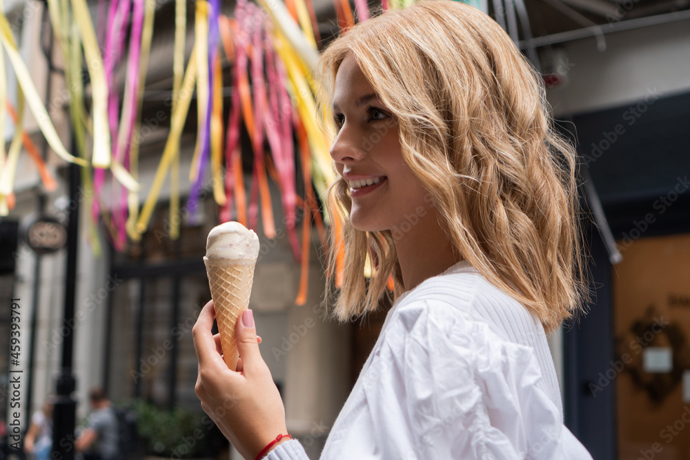 A beautiful teenage girl smiles on the colorful street with an ice cream cone in her hand.
