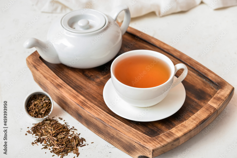 Wooden board with cup of tasty hojicha green tea and pot on light background Wooden board with cup of tasty hojicha green tea and pot on light background