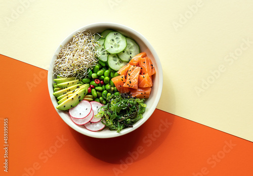 Asian trendy food, sushi poke bowl with edamame beans, cucumber, salmon, avocado, black and white sesame seeds, and seaweed. Great keto diet lunch or dinner. Colored paper background.