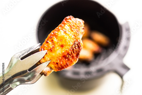 Baked chicken wings with tongs on blur Baked chicken wings in Air Fryer on white table background. cooking for low fat control weight. food for health concept. photo