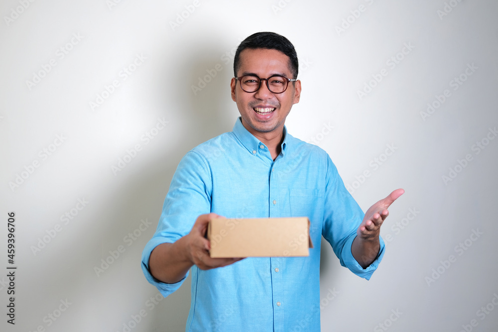 Adult Asian man smiling happy while giving a gift box Adult Asian man smiling happy while giving a gift box