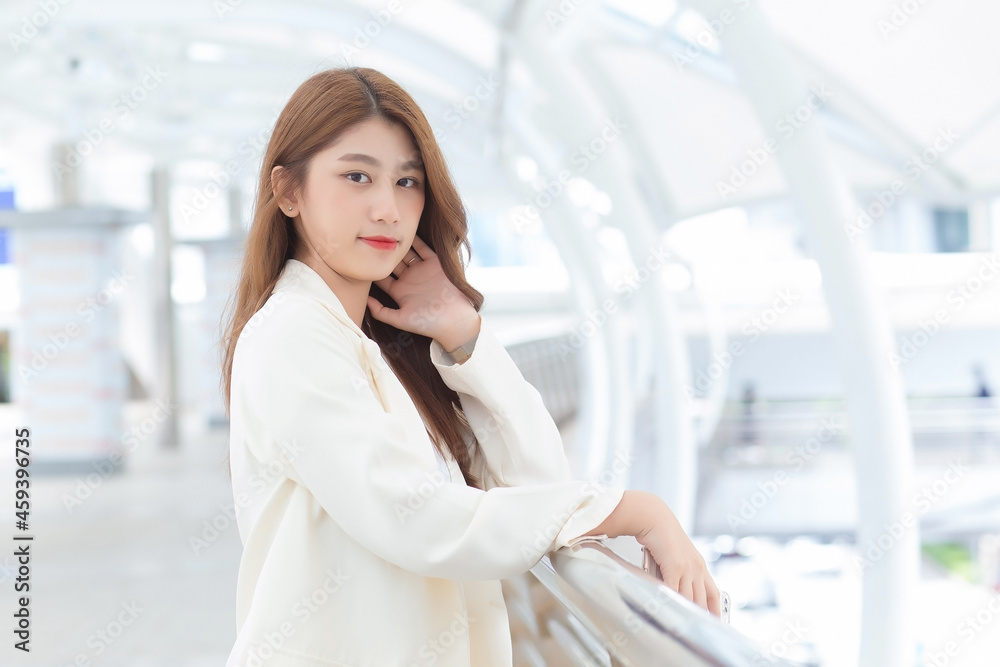 Portrait with blur background of long hair beautiful Asian professional woman in white suit with smiling face posing while working outside the office.