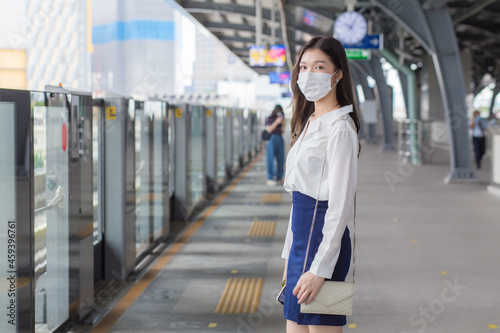 Asian professional business woman with long hair wears a mask is waiting to go to workplace or office by sky train in the New Normal lifestyle.