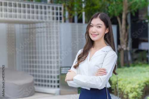 Asian businesswoman wearing a white shirt and standing with her arms crossed smile while working outside the office.