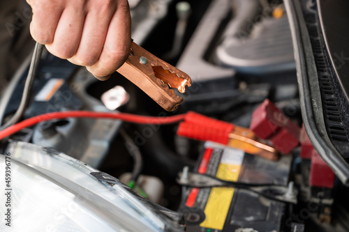 The mechanic connects the clamps to the discharged car battery.
