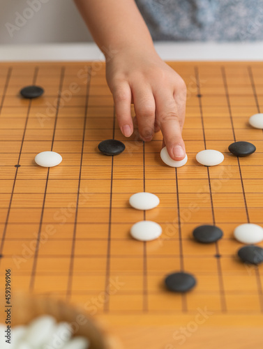 Child hand playing Go board game  white and black stones on the board game  wooden Asian classic game board with grid lines  Vertical image.