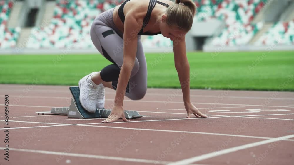 Young female sprinter is preparing for the start of a training run in short-distance, professional track runner at a stadium, a tense moment, handheld.