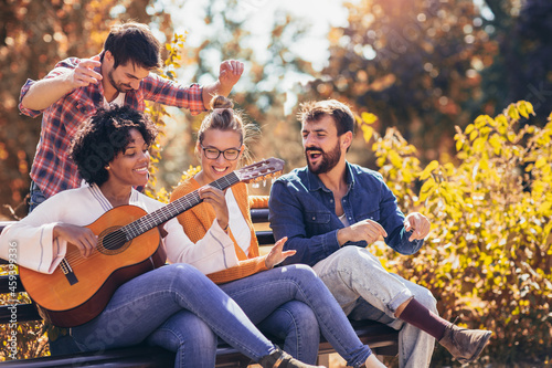 Group of young people hangout in the park.They sitting on bench ,singing and playing guitar.
