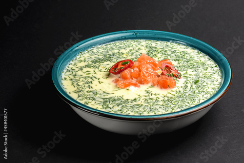 Summer cold yogurt soup okroshka with salmon served in a blue bowl over black background. photo