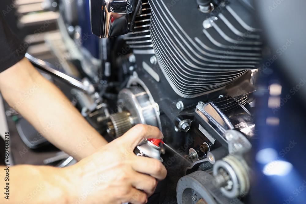 Master locksmith puffs liquid on motorcycle engine in garage closeup