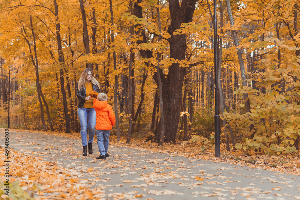 Mother and son walking in the fall park and enjoying the beautiful autumn nature. Season, single parent and children concept. Mother and son walking in the fall park and enjoying the beautiful autumn nature. Season, single parent and children concept.