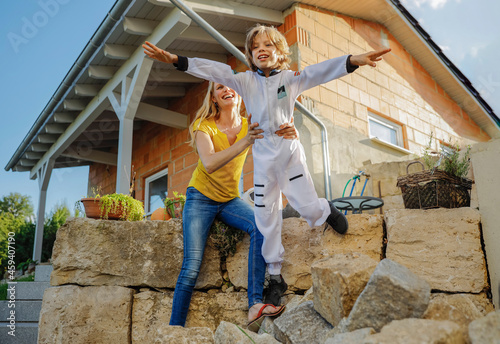 Cheerful mother assisting aspiring astronaut son in flying